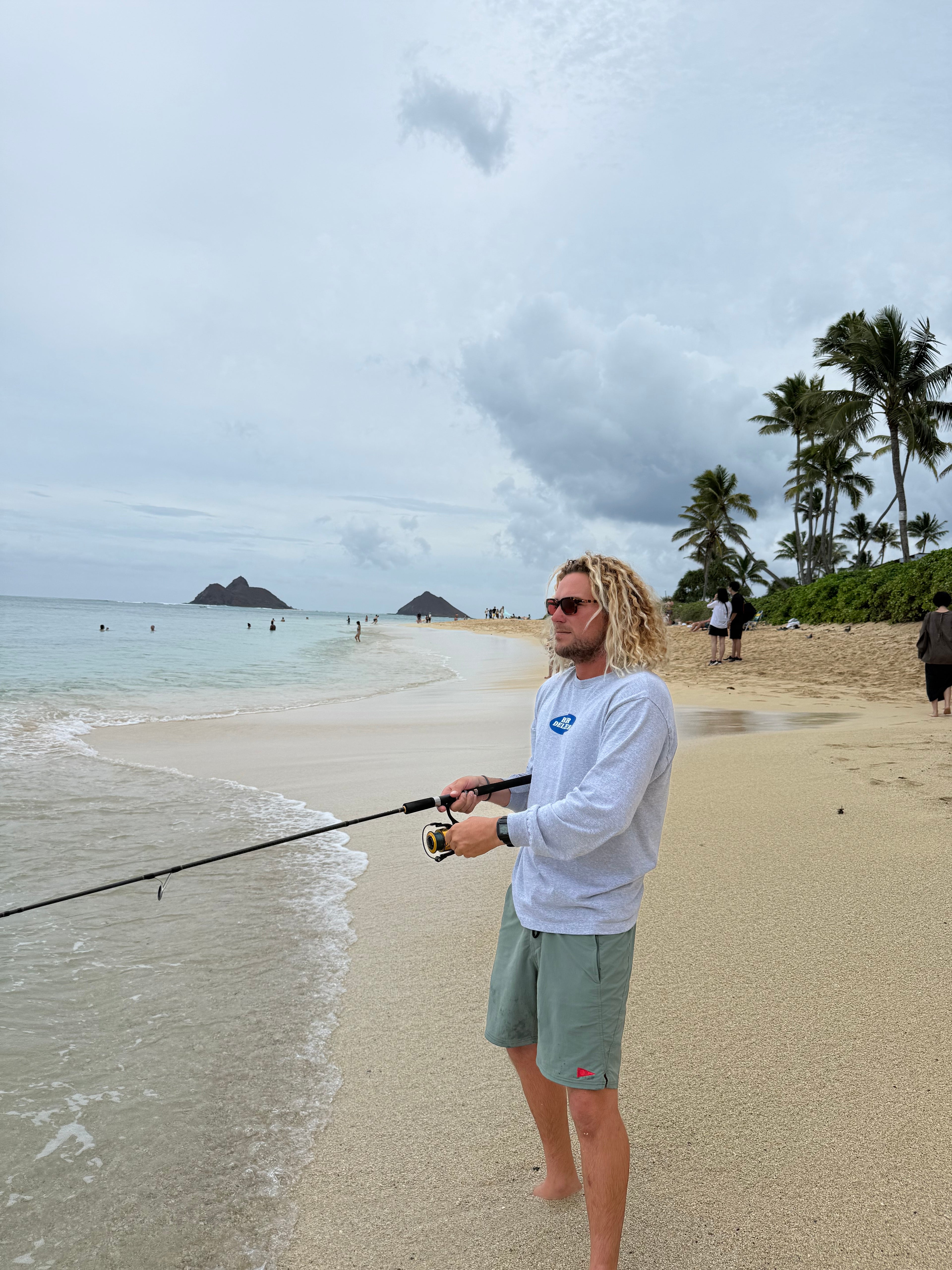 Person fishing on a sandy beach with palm trees in the background